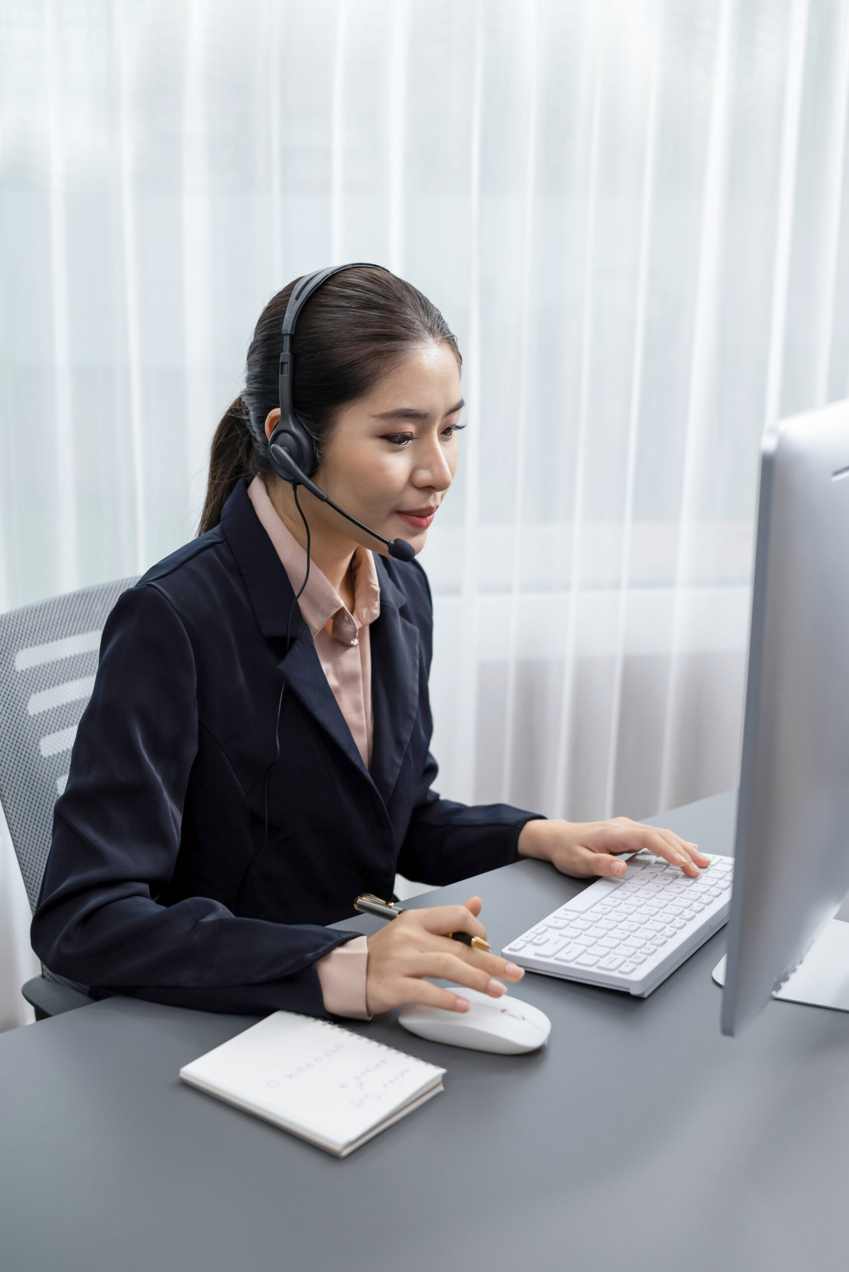 enthusiastic asian call center with headset and microphone working on her laptop